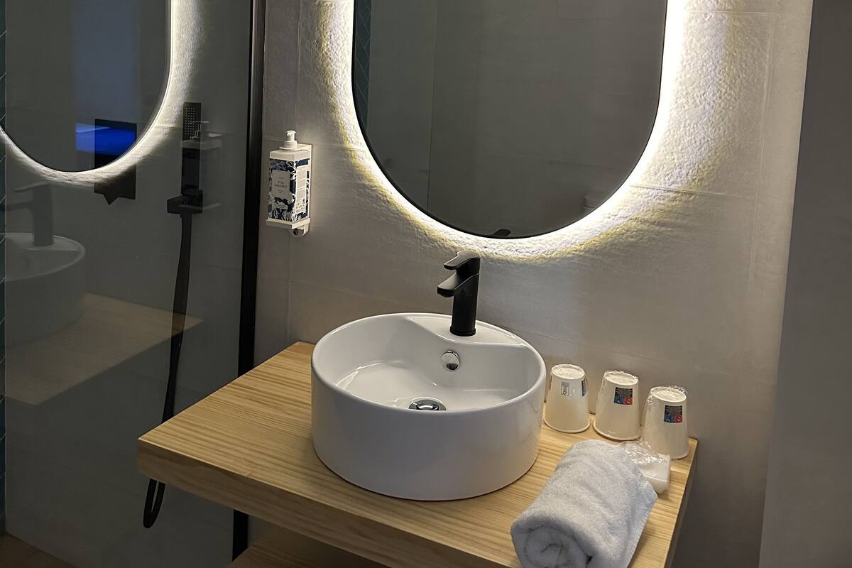 A modern bathroom with a large oval mirror, a white sink, and a wooden vanity.