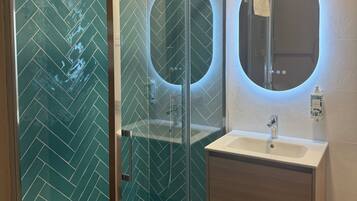 Un baño moderno con ducha envuelta en vidrio, tocador con lavabo y espejo con luz circular.