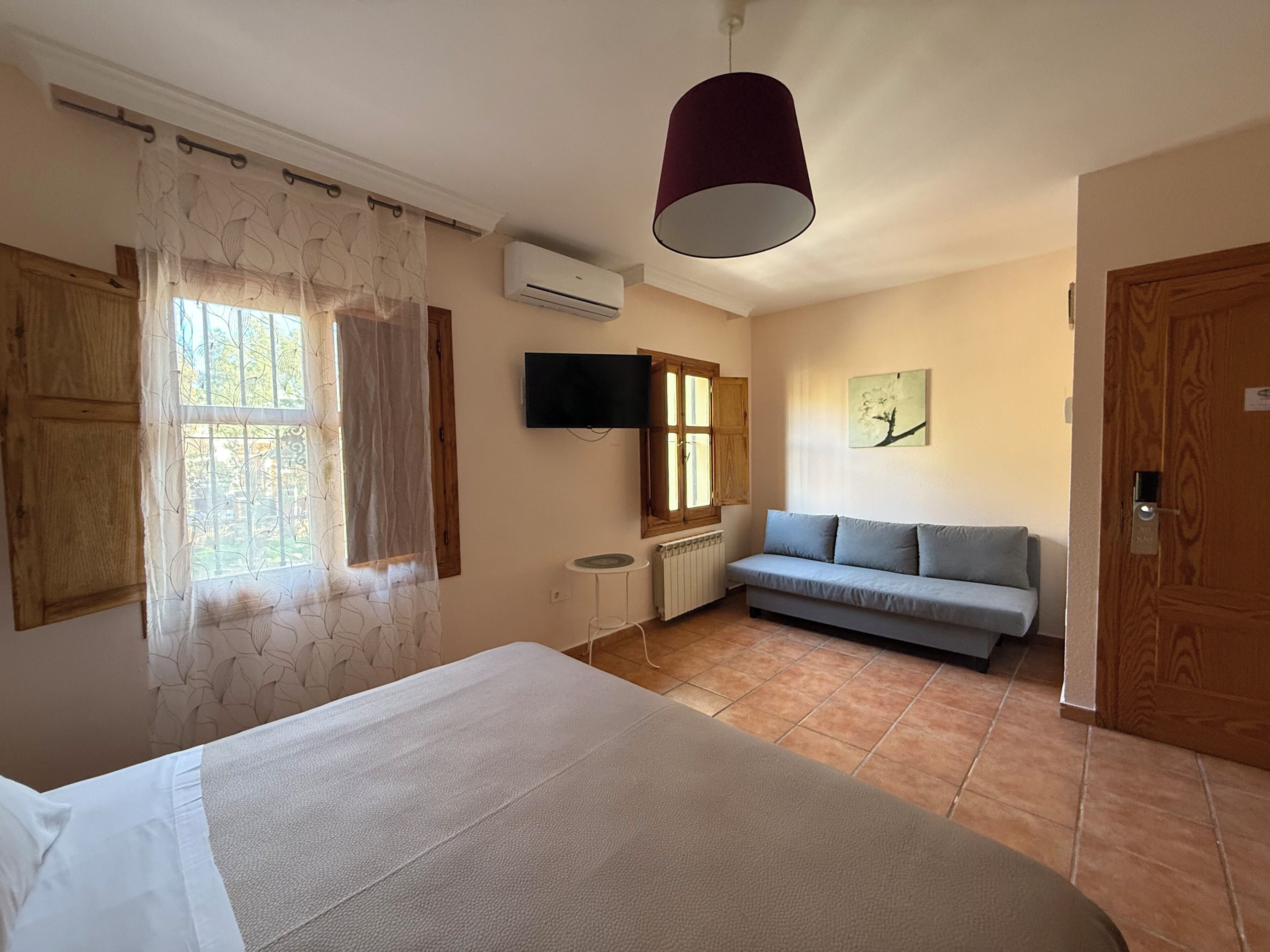 Una habitación con cama, sofá, televisor y ventana con cortinas.