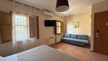 Quarto com cama, sofá, televisão e janela com cortinas.