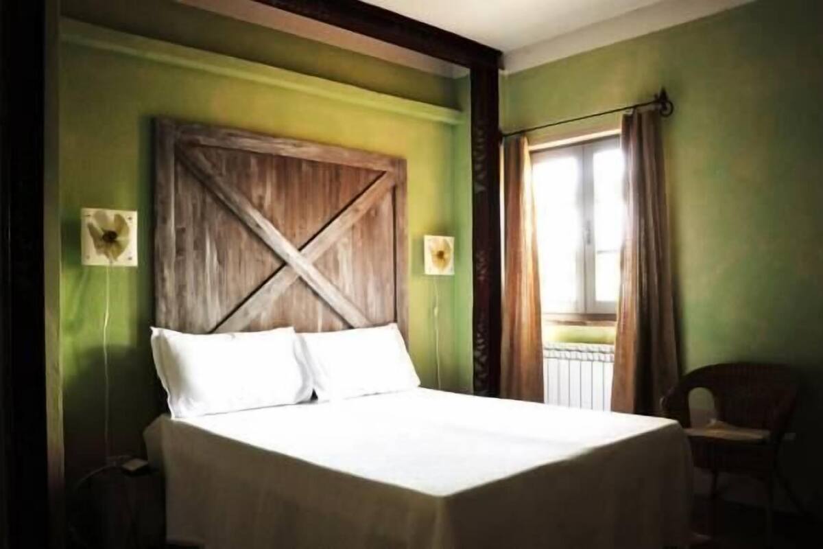 Een bed met een houten hoofdbord, een stoel en een raam met gordijnen.
