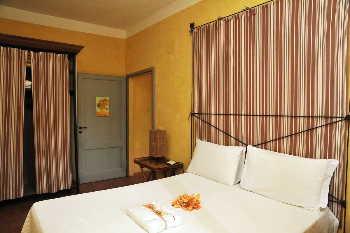 Een hotelkamer met een bed, gordijnen, een nachtkastje en een stoel.