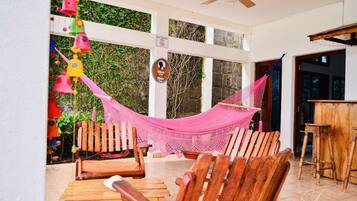 A hammock chair, wooden chairs, and a table in a room with a ceiling fan.