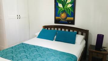 A bed with blue and white bedding, a wooden headboard, and a small bedside table with a purple vase.