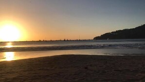 En strand med solnedgang over horisonten, roligt vand og en fjer borte kystlinje.