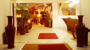 A reception area with a glass partition, potted plants, a red carpet, and a bench. - Nomad Suites Residence (Libreville)