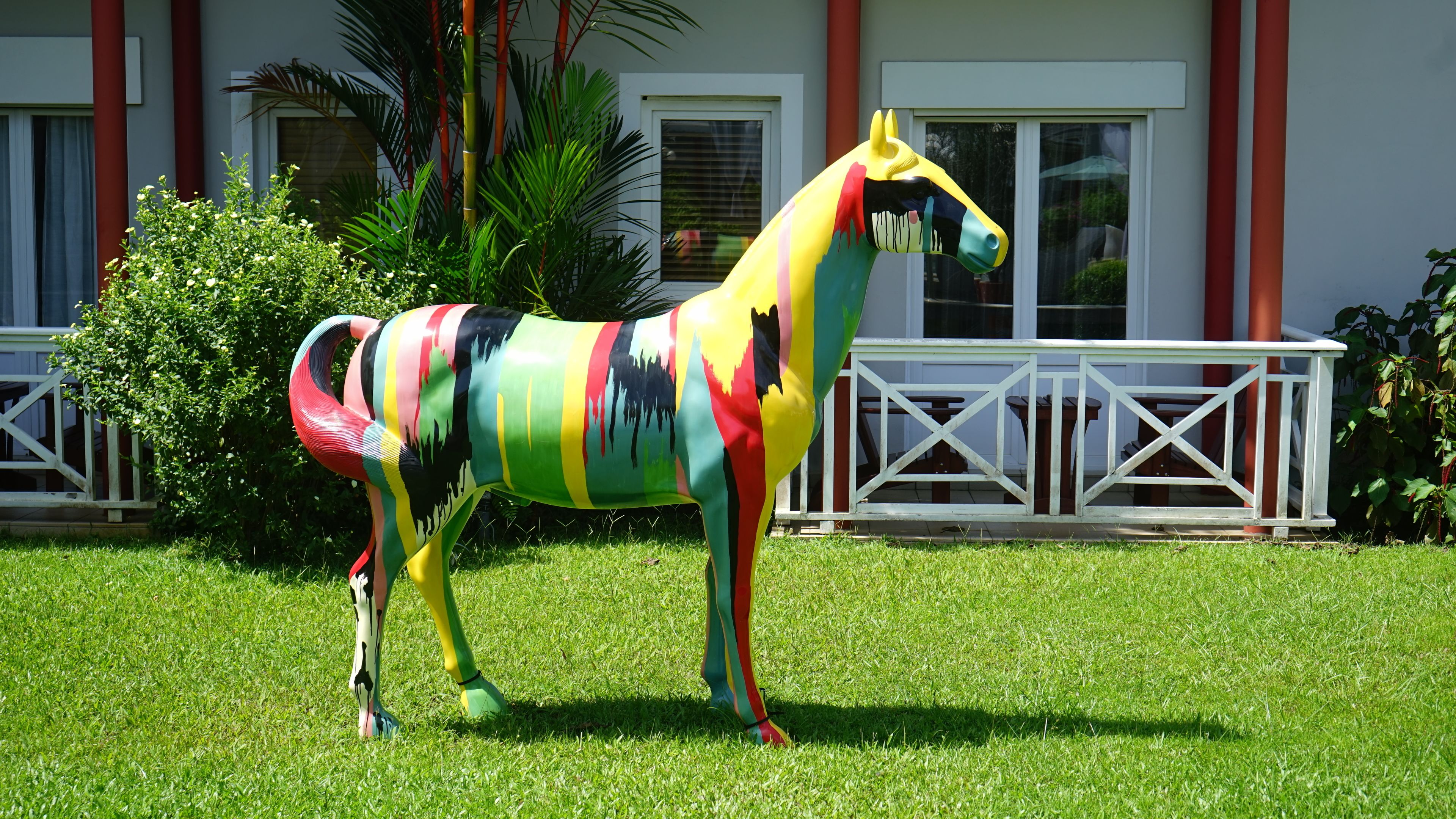 A colorful horse statue in a grassy area with a building in the background.