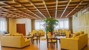 A spacious room with wooden ceiling beams, yellow sofas, and a central potted plant. - Nomad Suites Residence (Libreville)