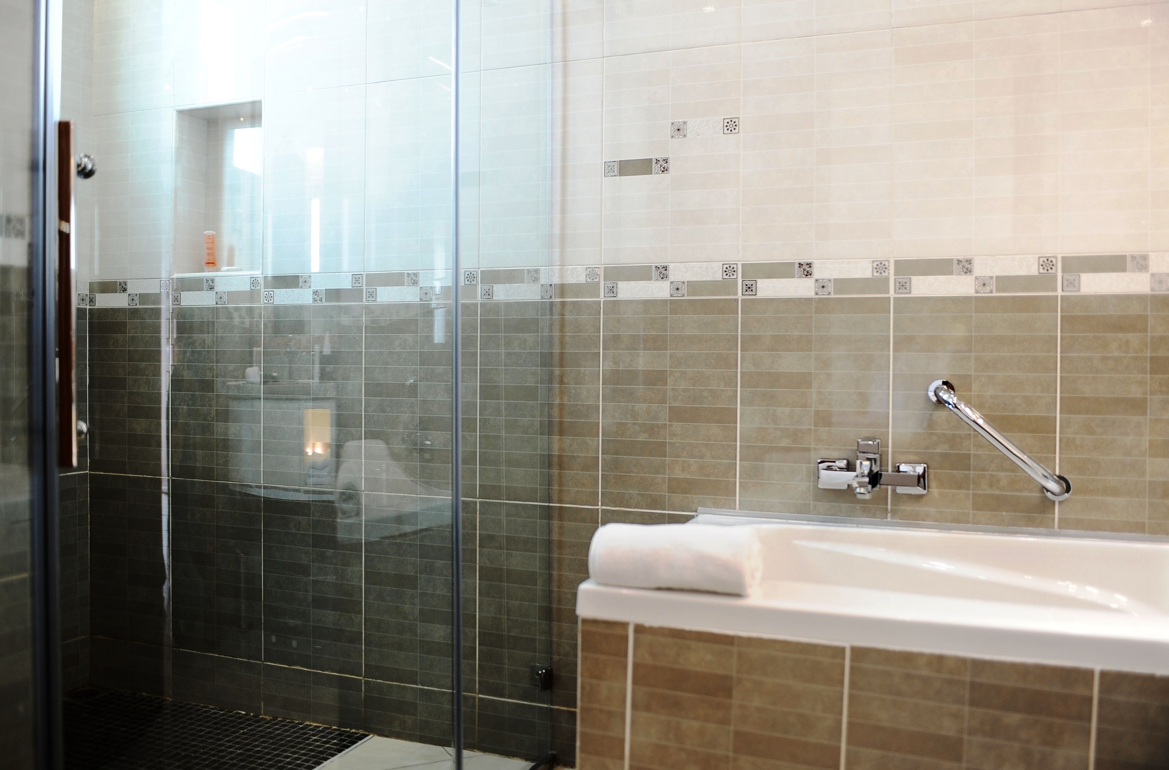 Une salle de bain moderne dotée d’une douche à parois de verre, d’une baignoire avec un robinet chromé et d’un mur carrelé orné de motifs décoratifs.