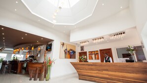 A modern hotel lobby with a wooden reception desk, a bar area, and a high ceiling with recessed lighting. - Nomad Suites Residence (Libreville)