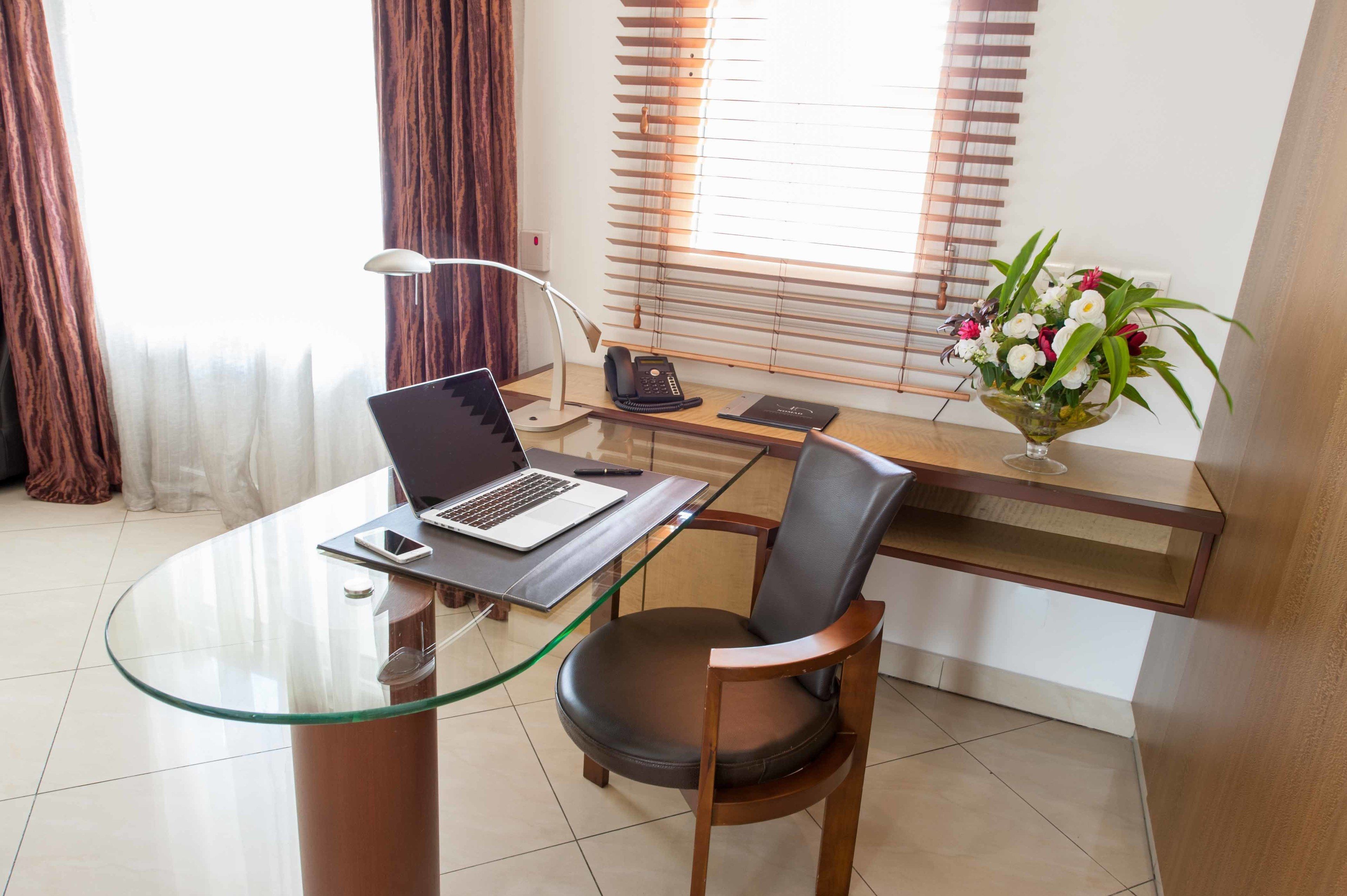Un espace de bureau moderne avec un bureau en verre, un ordinateur portable, un téléphone et une chaise.