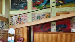 A hotel lobby with a staircase, wooden reception desk, and colorful murals. - Park Place Hotel (Siguatepeque)