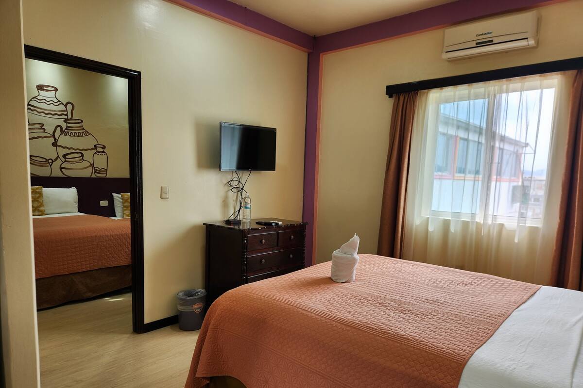 A hotel room with a bed, a dresser, a television, and a window with curtains.