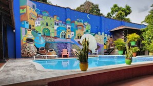 A swimming pool with steps leading up to it, surrounded by colorful murals and potted plants. - Park Place Hotel (Siguatepeque)