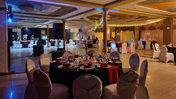 A banquet hall with round tables set for a formal event, featuring white chairs with bows, a stage area, and a decorative ceiling. - Park Place Hotel (Siguatepeque)