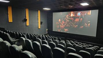 Ein Kino mit Reihen schwarzer Sitze, einer großen Leinwand und dekorativen Wandverkleidungen.