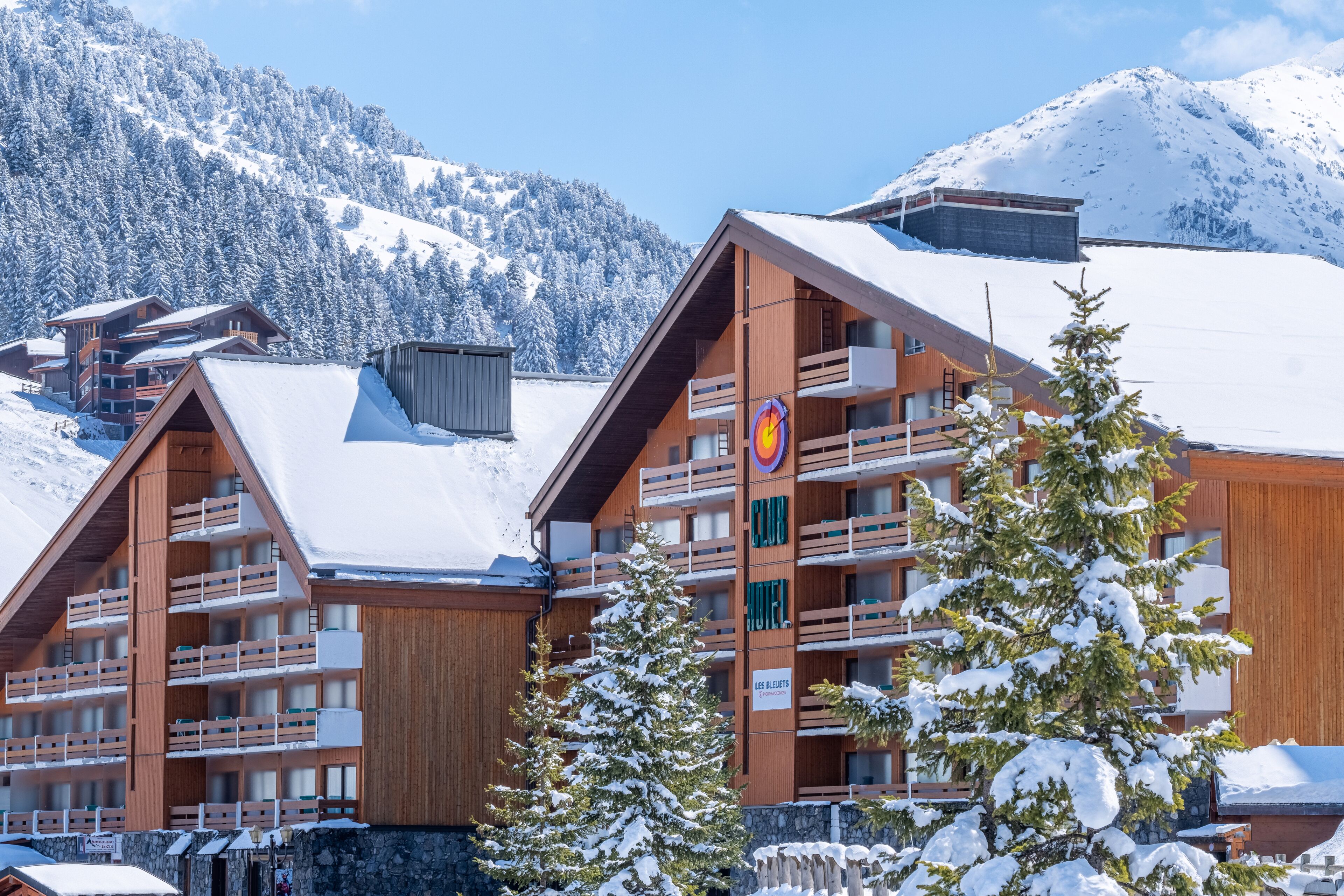 A wooden chalet-style hotel with multiple balconies and a ski slope in the background.
