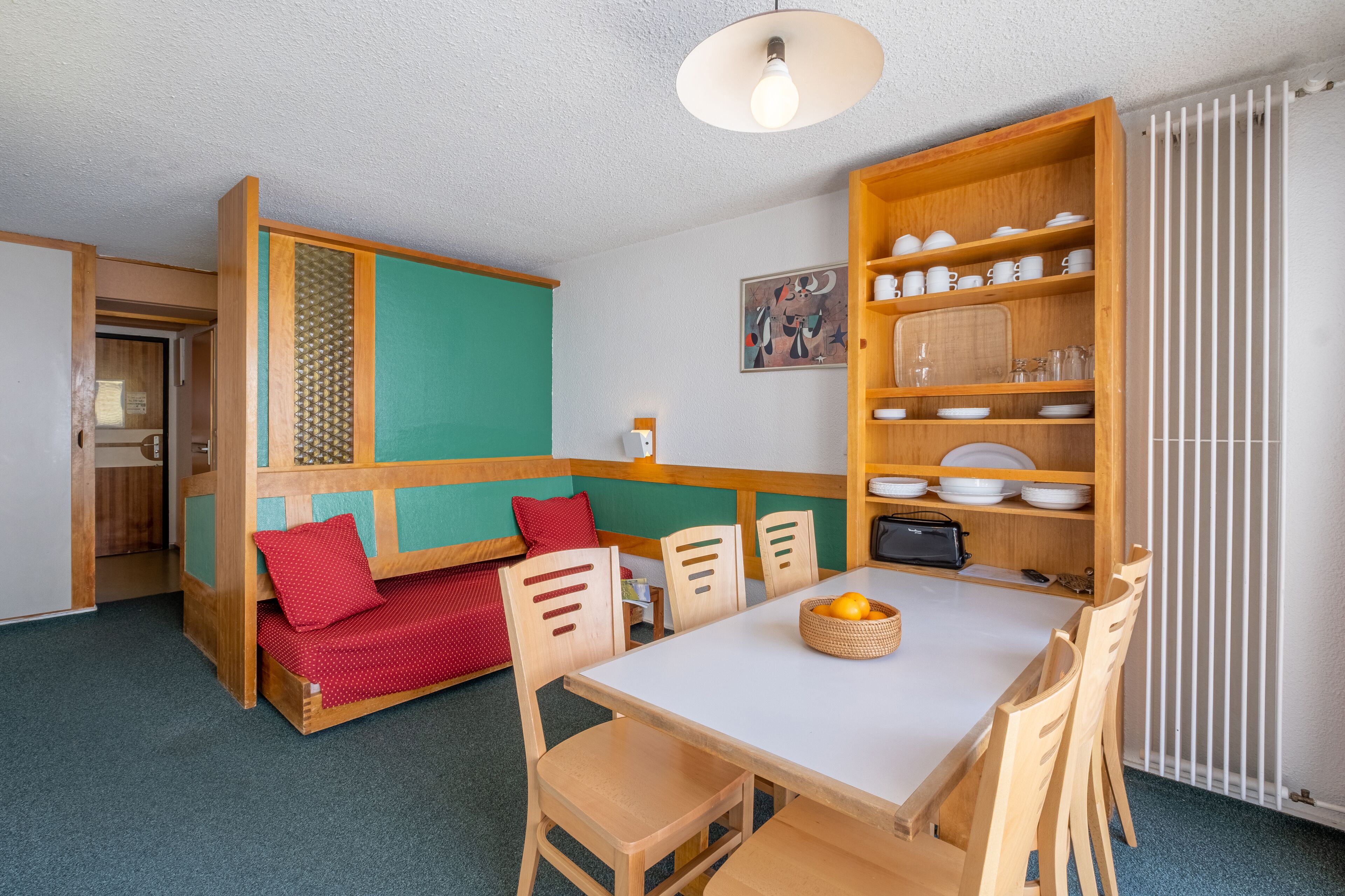 Une pièce de taille modeste comprenant une table à manger, des chaises, un petit canapé, une bibliothèque en bois et un radiateur.