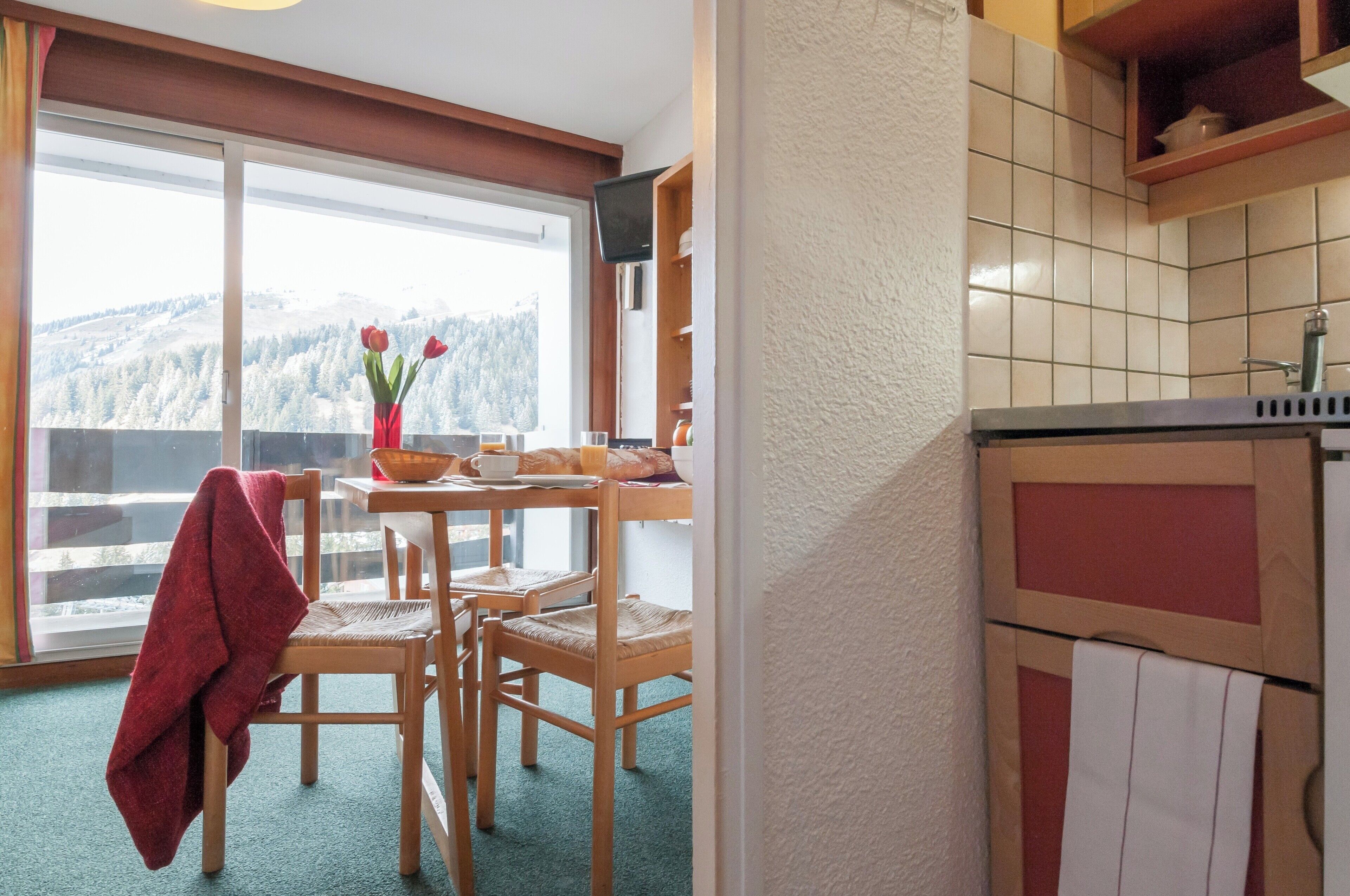 A kitchen with a view of a snowy mountain, a dining table with chairs, and a red towel hanging on a chair.