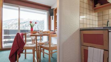 Une cuisine donnant sur une montagne enneigée, une table à manger avec des chaises, et une serviette rouge accrochée à une chaise.