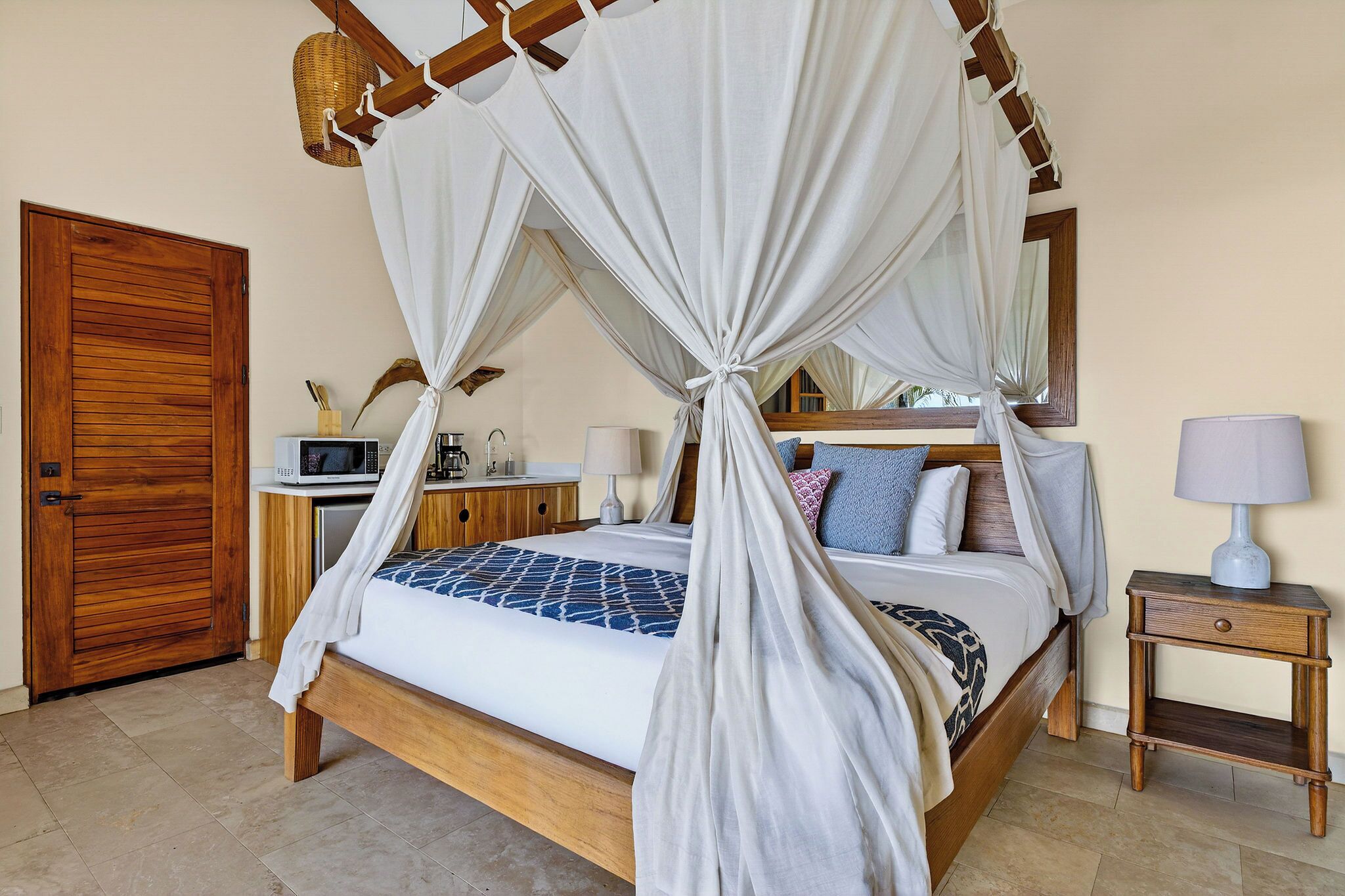 A four-poster bed with a canopy, a wooden door, a bedside table with a lamp, and a small cabinet.