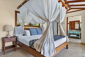 A four-poster canopy bed with a wooden headboard, a nightstand with a lamp, and a vanity with a mirror. - Ocio Villas Mal Pais (Cóbano)