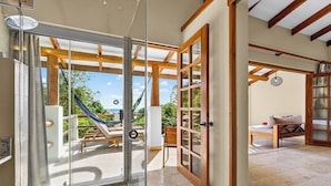 Un intérieur moderne avec une porte vitrée donnant sur un balcon, des poutres en bois et une vue sur l’extérieur.