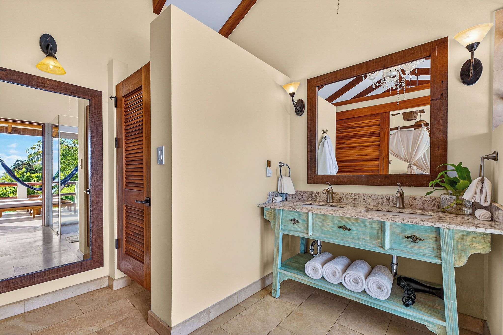 A bathroom with a wooden door, a large mirror, a sink with a marble countertop, and a towel rack with towels.