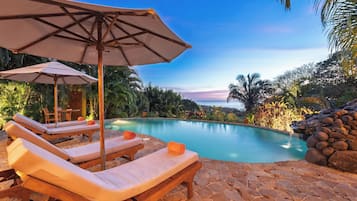 Una piscina al aire libre, sombrillas, sillones reclinables de piscina