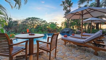 Un área de piscina con sillones de descanso, una mesa y sombrillas.