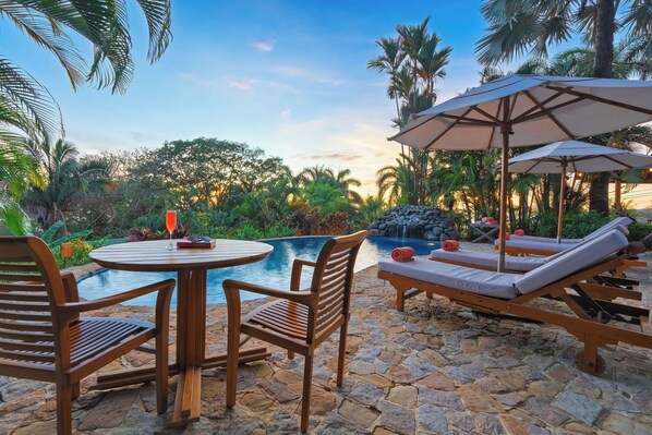 A pool area with lounge chairs, a table, and umbrellas.