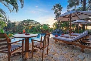 Un área de piscina con sillones de descanso, una mesa y sombrillas.