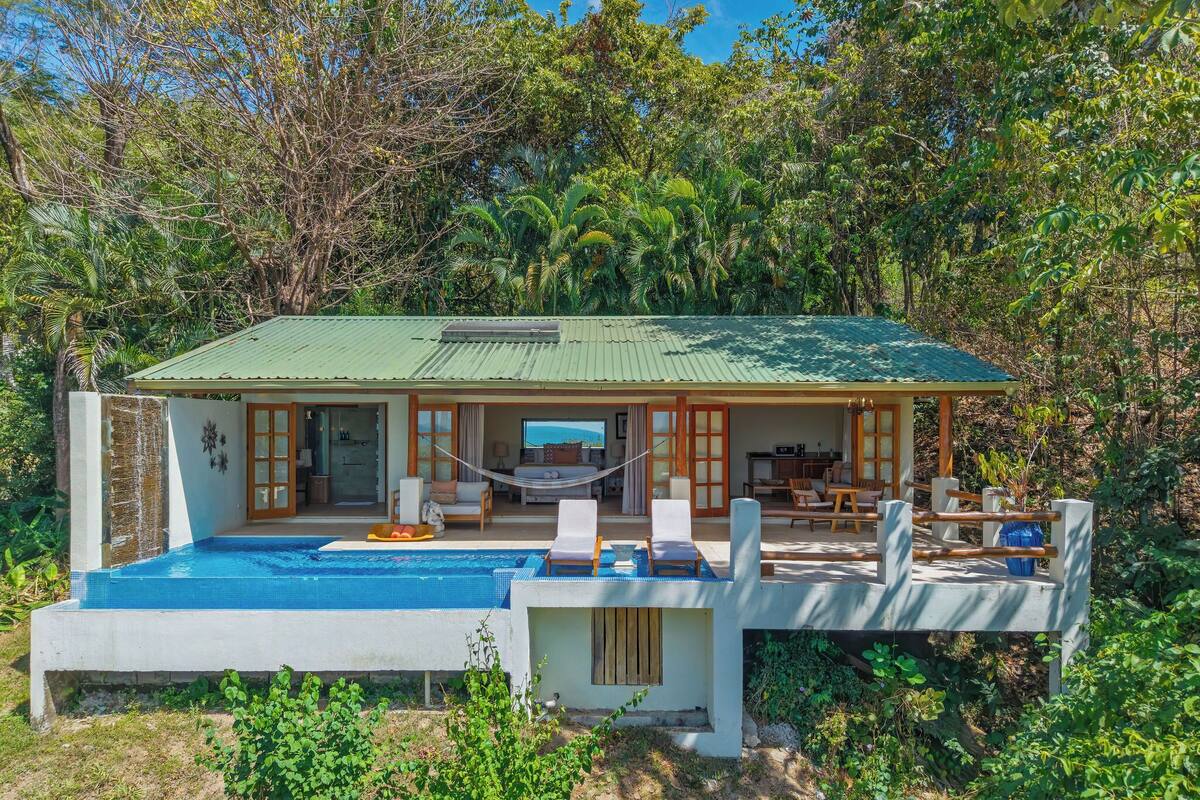 Ein zweistöckiges Haus mit Swimmingpool, Essbereich und Blick auf den Ozean.