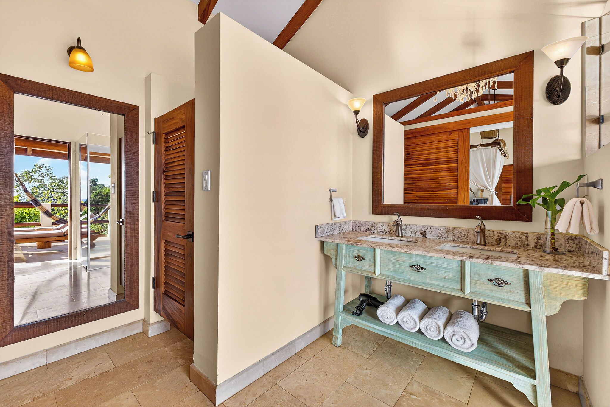 A bathroom with a wooden door, a sink with a mirror, and towels on a shelf.