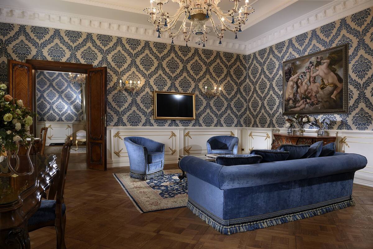 A room with a blue sofa, wooden chairs, a dining table, and a chandelier.