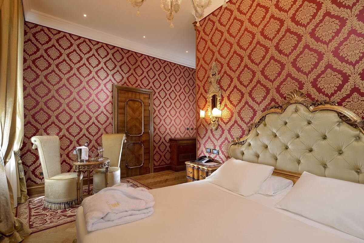 A hotel room with a large bed, a sitting area with a chair and a small table, and a mirror.