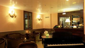 Una habitación con piano de cola, zona de estar y bar con botellas.