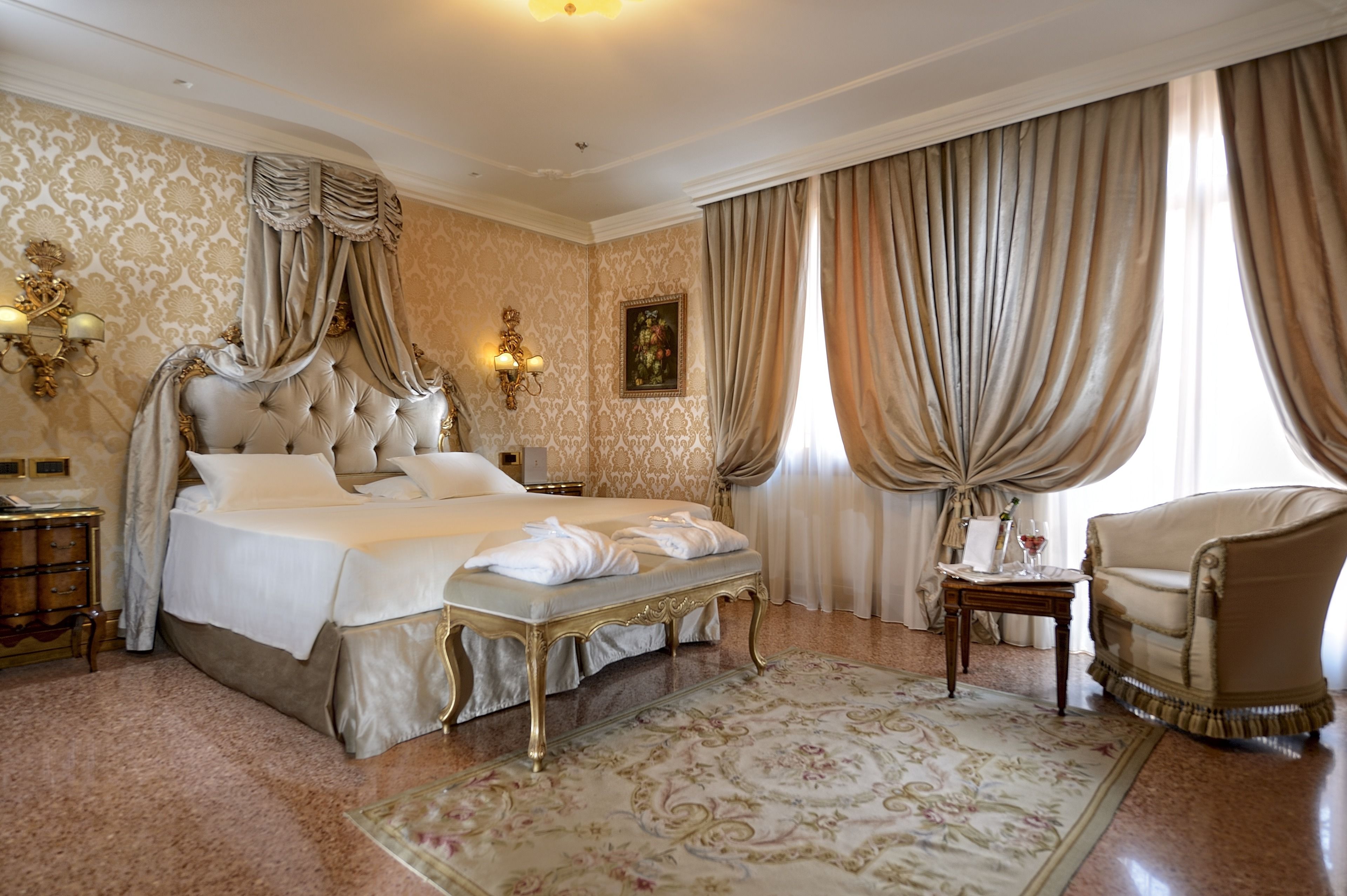 Un dormitorio lujoso con una cama grande, un chaise-lounge y un candelabro clásico.