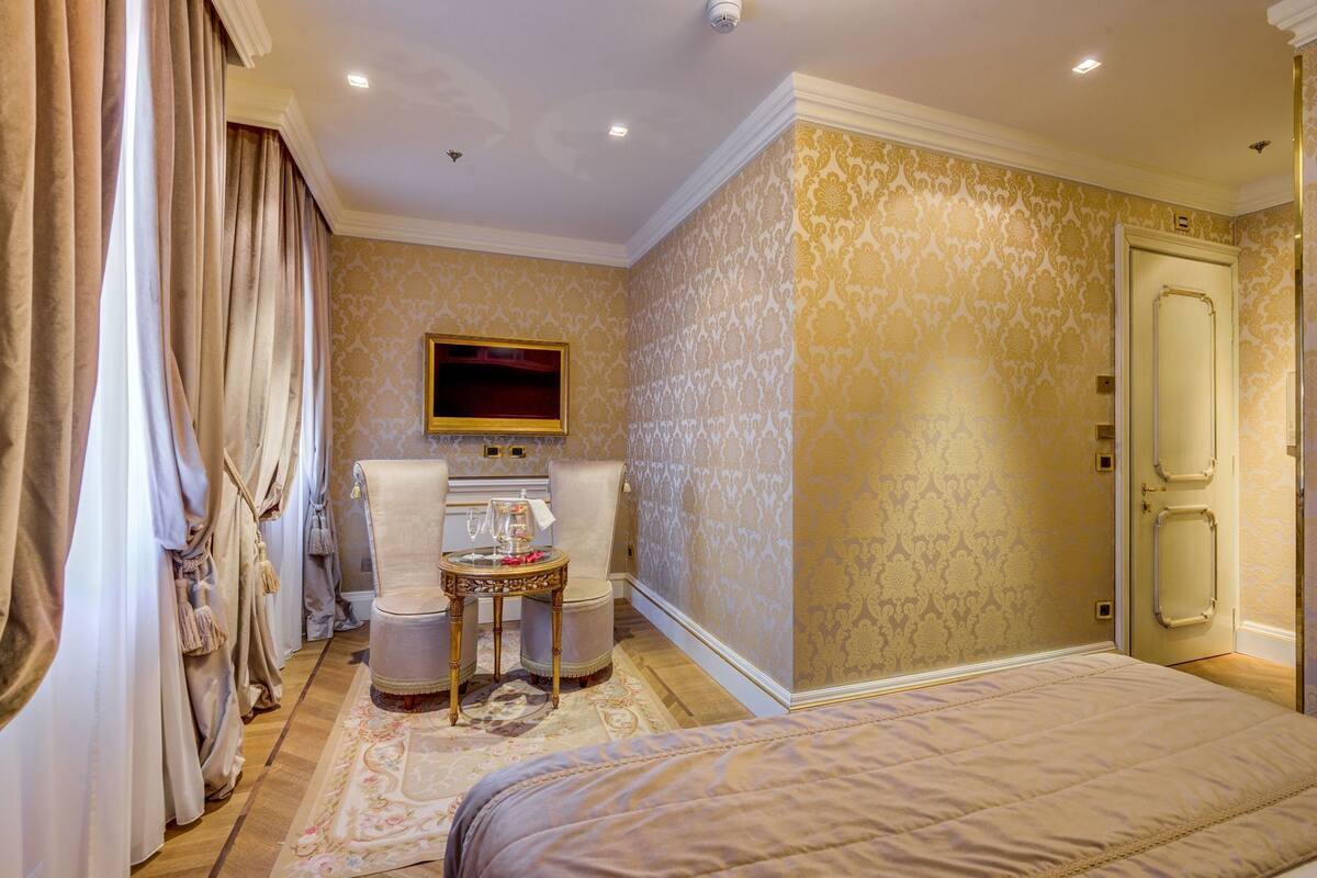 A hotel room with a bed, two chairs, a small table with a glass, and a television on the wall.