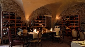 Une cave à vin aux murs en briques en arc de cercle, avec des étagères à vin en bois et une table à manger dressée pour quatre personnes, agrémentée de bougies.