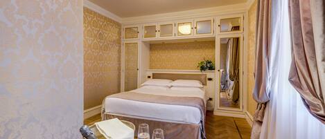 A hotel room with a large bed, a mirror above the bed, a round table with a tray, and a chandelier.