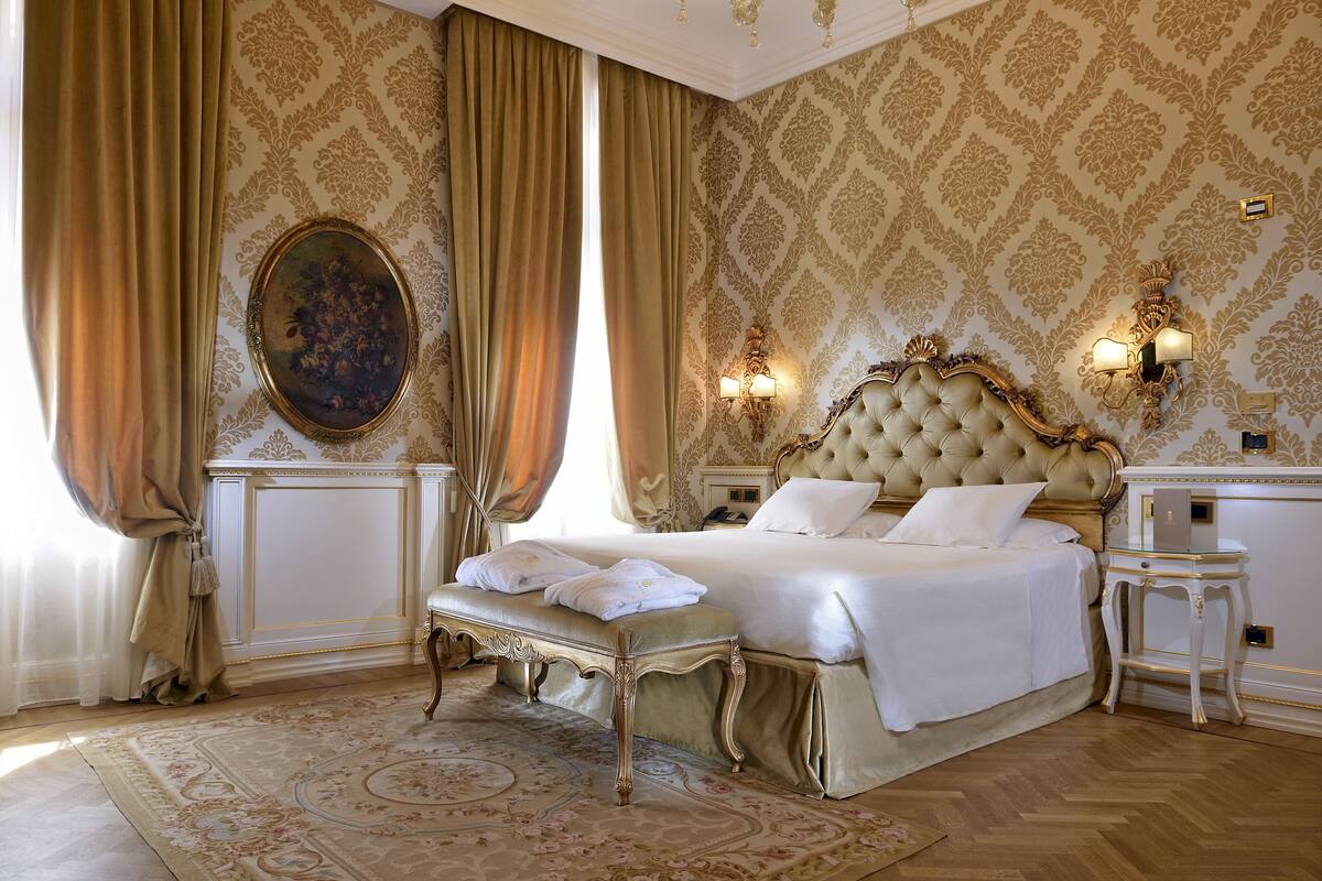 A luxurious bedroom with a large bed, ornate headboard, and a classic chandelier.