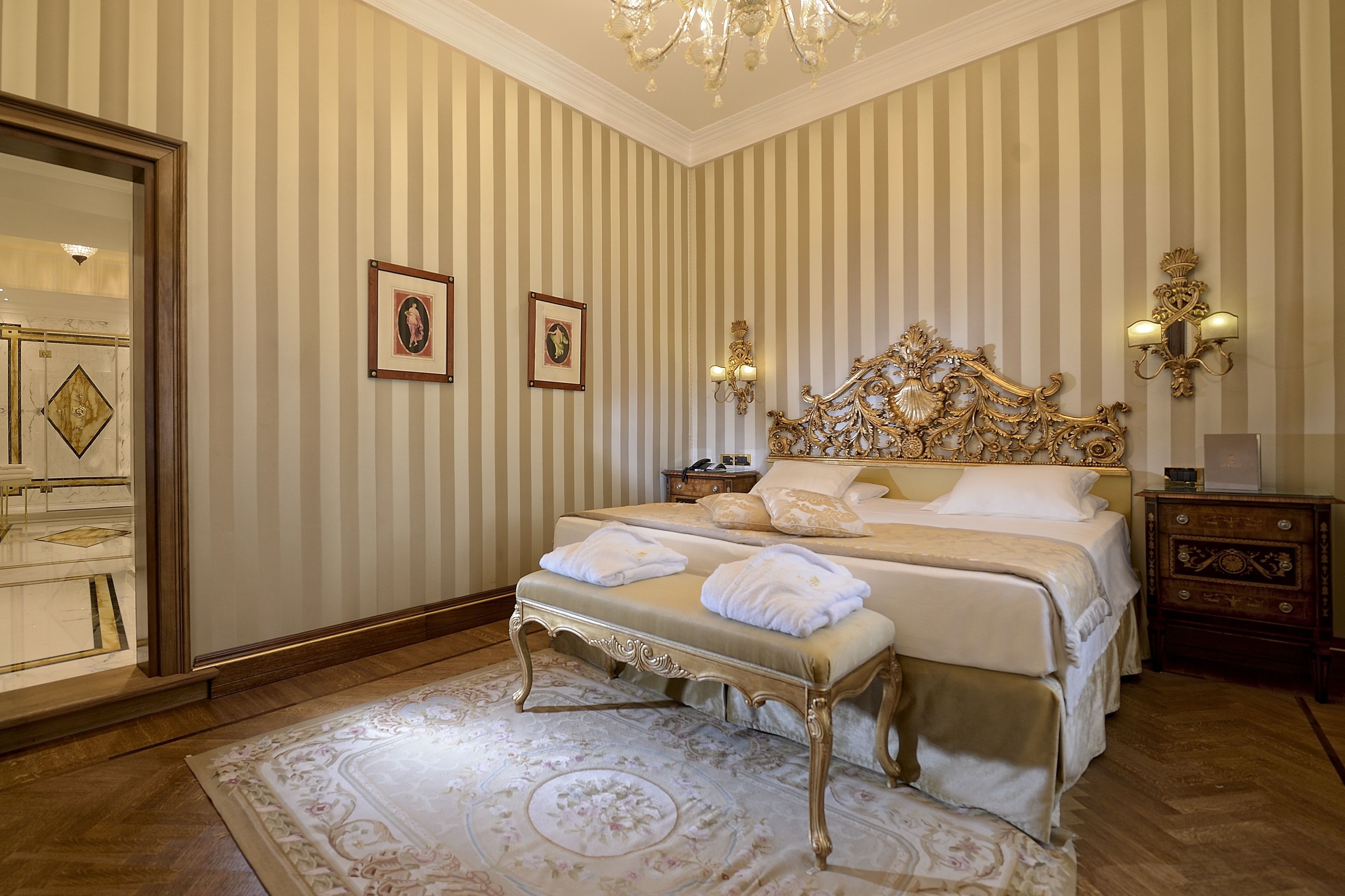 A classic hotel bedroom with a large bed, ornate headboard, and a chandelier.