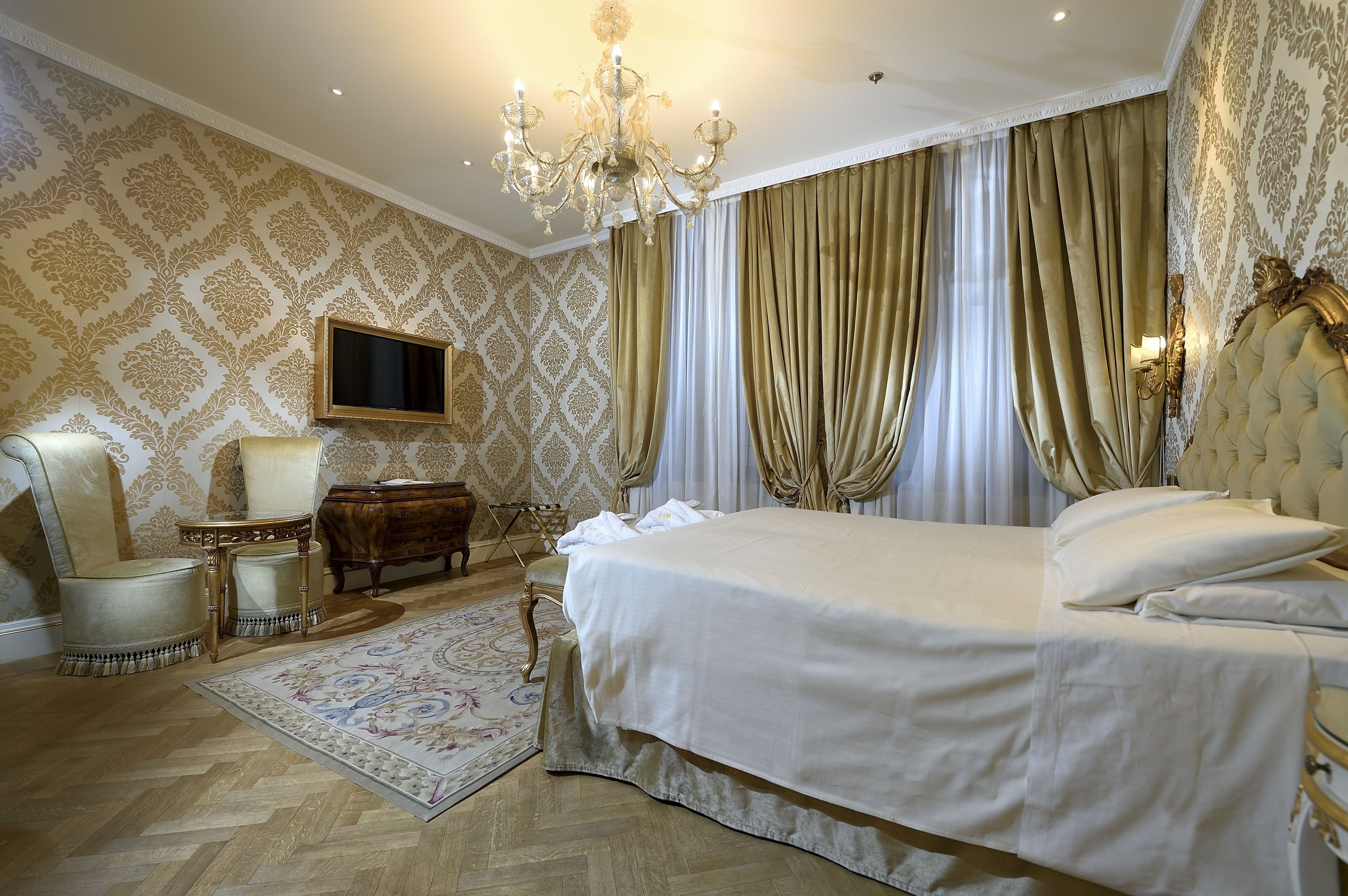 Quarto com uma cama grande, um candelabro, uma televisão e papel de parede ornamentado.