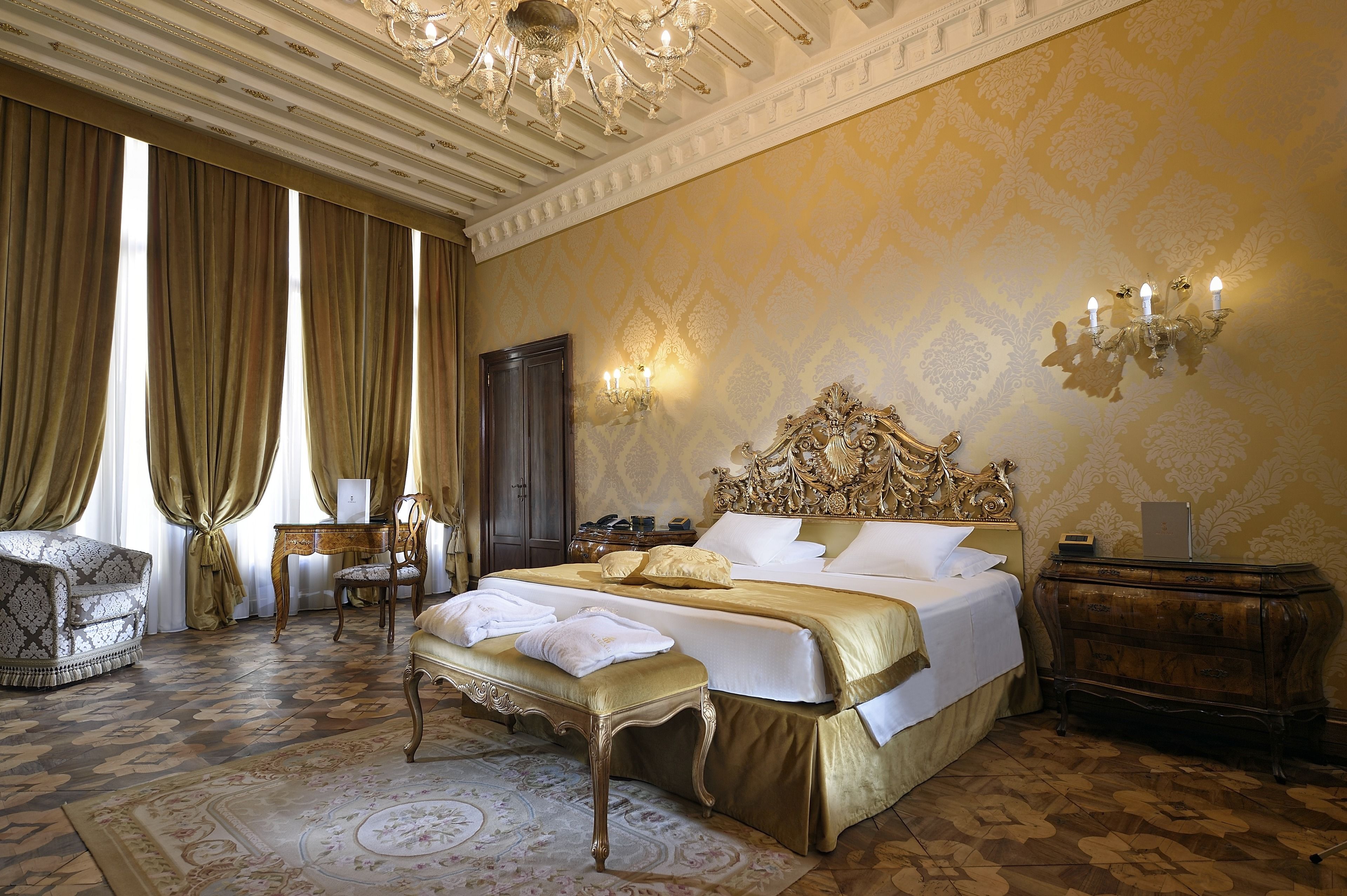 Um quarto luxuoso com uma cama grande, cabeceira ornamentada e um candelabro.
