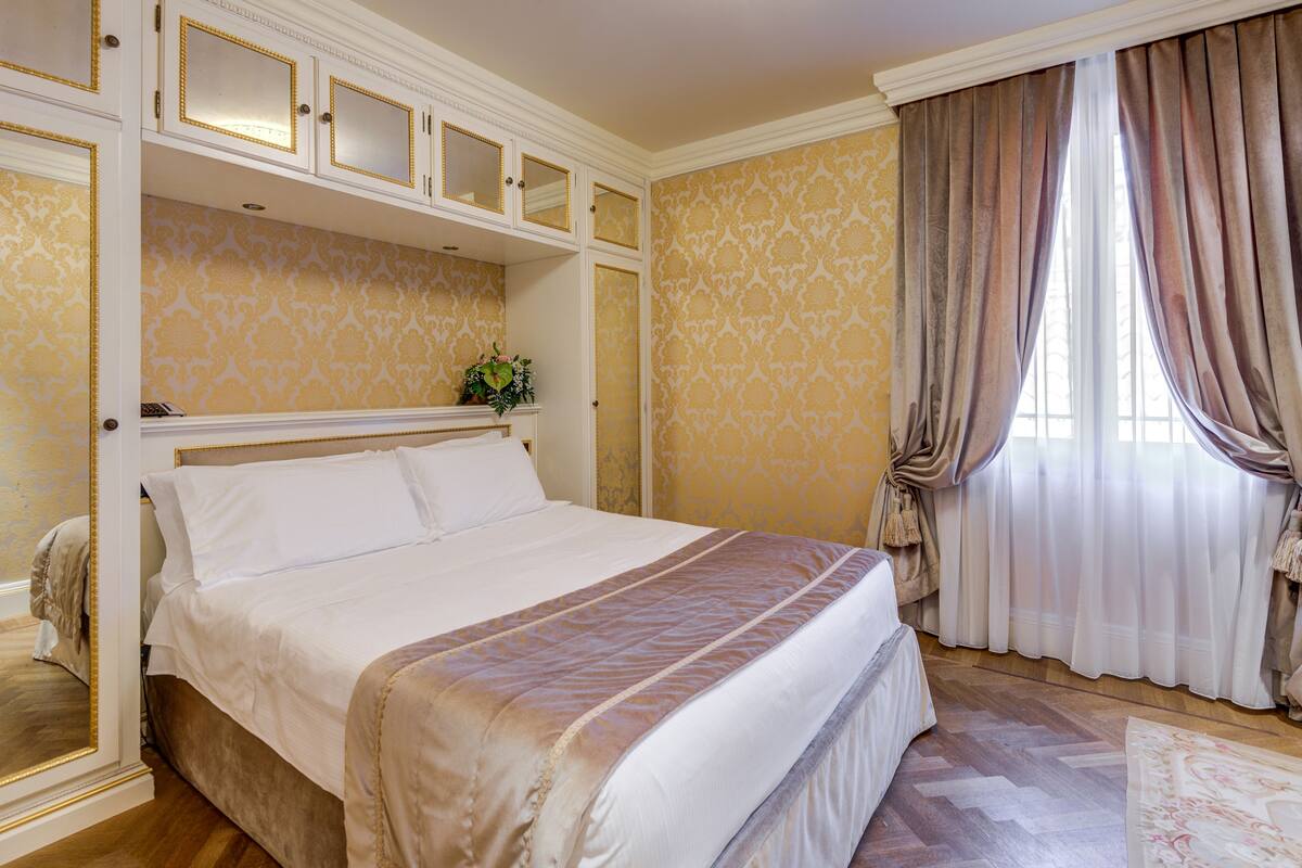 A bedroom with a large bed, a mirror, and a window with curtains.