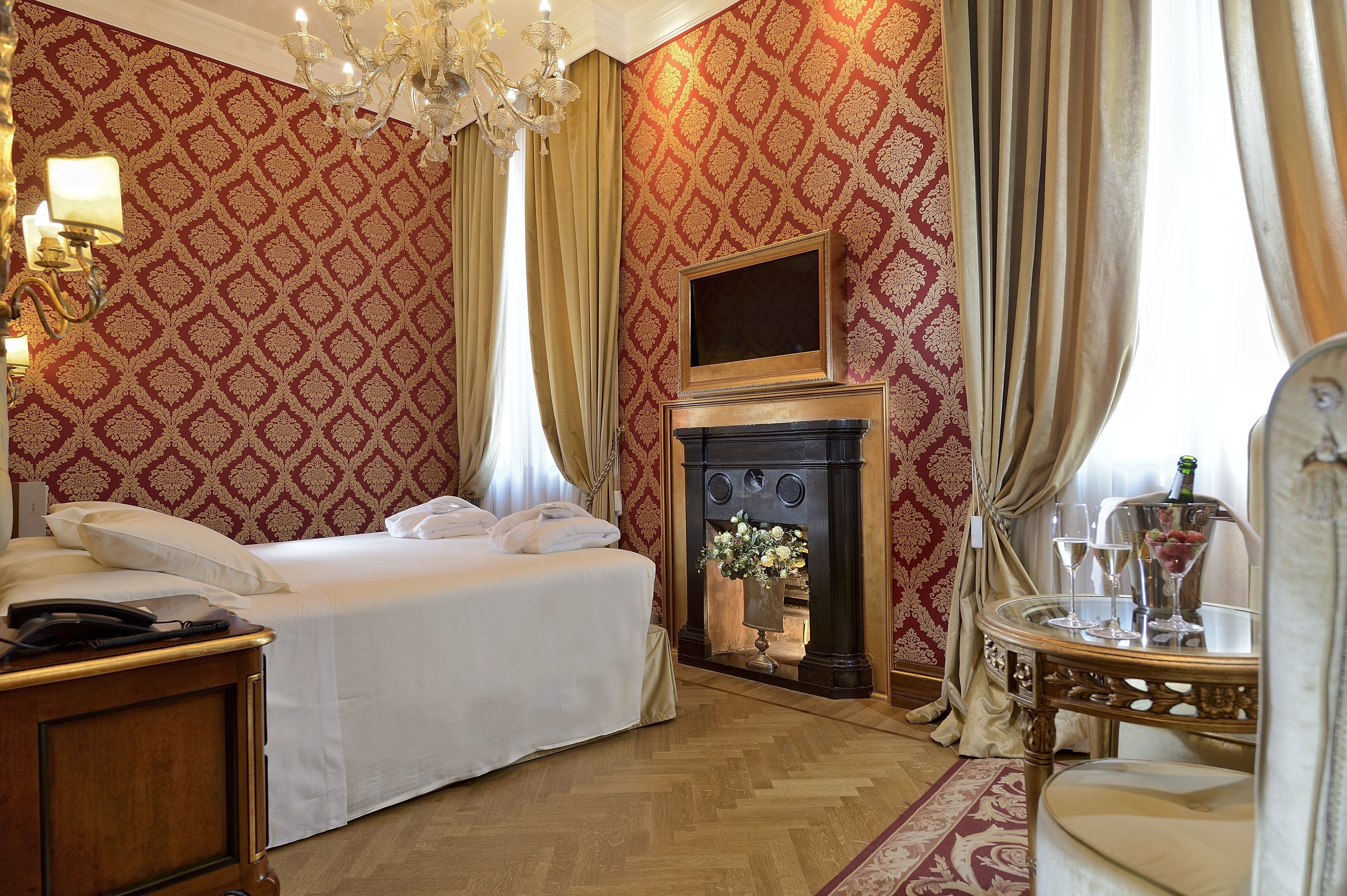 Ein Hotelzimmer mit Bett, Kamin, einem Tisch mit Gläsern und einer Chandelier.