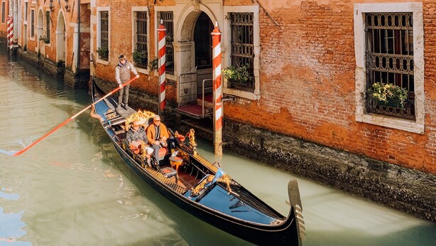 Une gondole sur un canal de Venise, en Italie, avec un bâtiment doté de fenêtres en arc de cercle et d’un balcon.