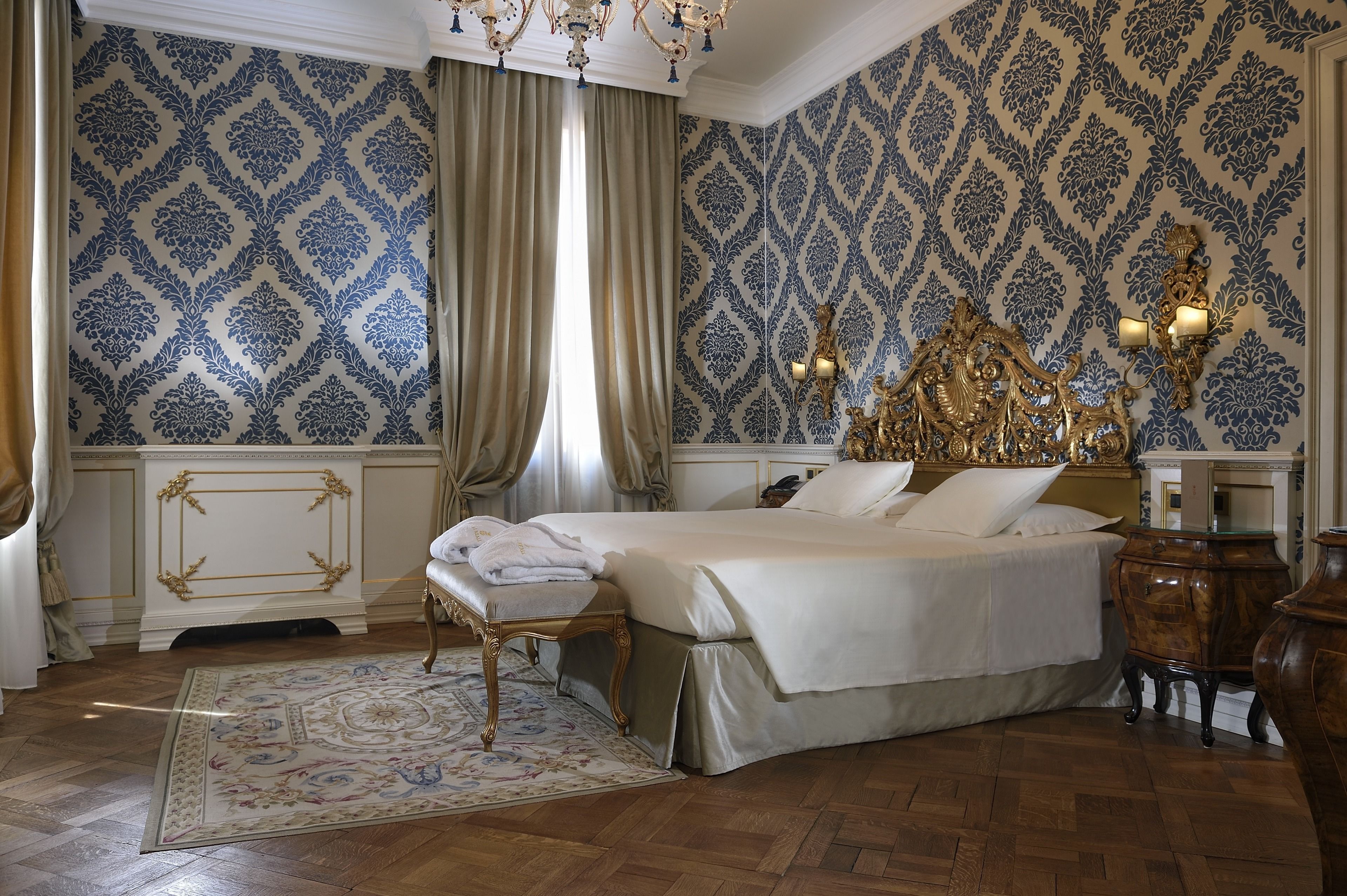 Un dormitorio clásico con una cama grande, cabecera decorada y un tapete ornamental.