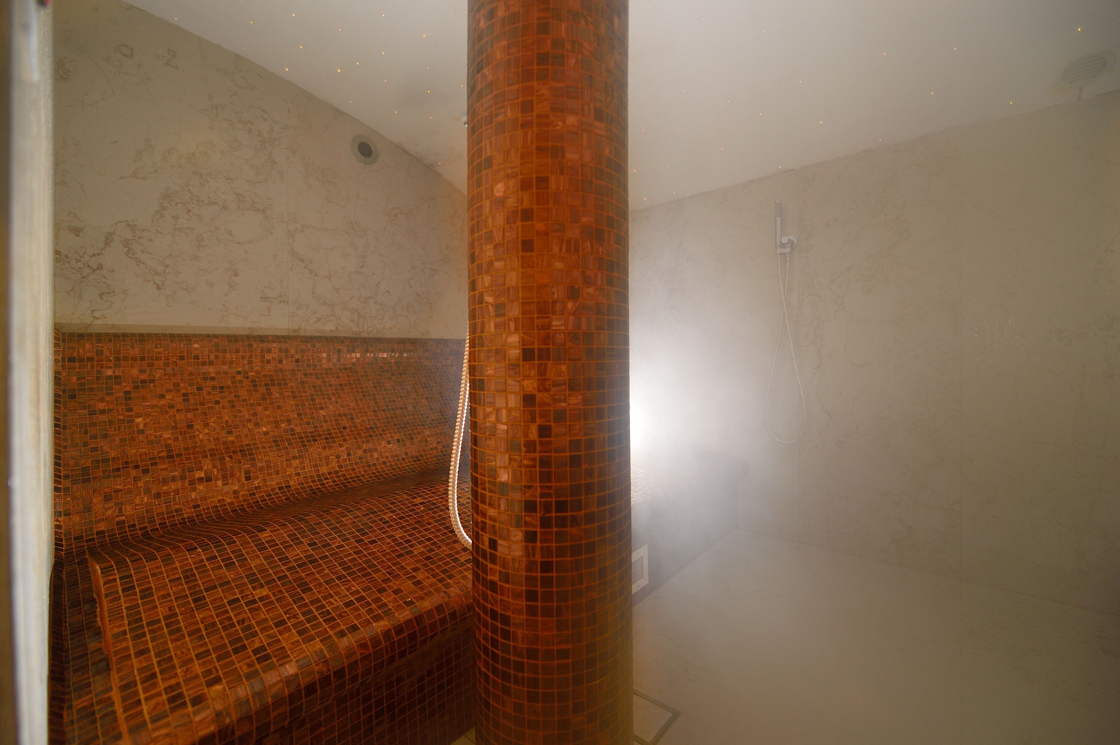Une salle de bain avec un banc carrelé, une colonne ornée de mosaïques et un espace douche.